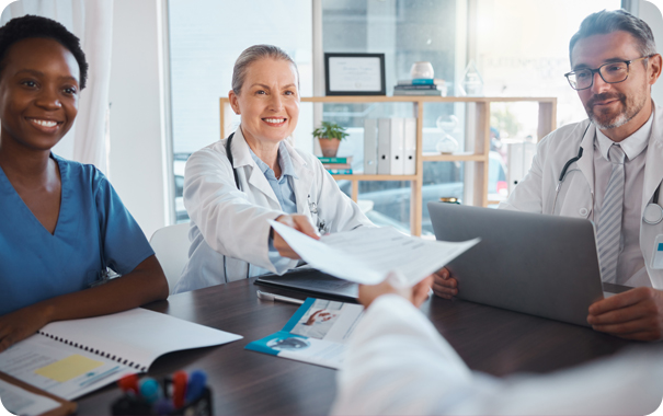 Smiling female nurse and two male and female doctors reviewing documents together during an Excellence Billing consultation for home health and hospice provider revenue cycle management.