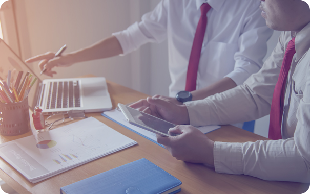 Describe what's actually happening for screen readers, weaving in keywords. Two Excellence Billing professionals in white shirts and red ties analyzing financial pie charts and claims data on a laptop and tablet for hospice and home health provider billing and compliance.