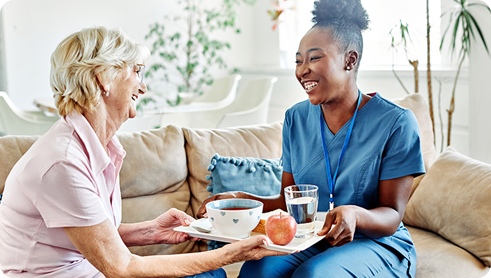 Home health care worker serving a meal to a senior woman in her home, supported by Excellence Billing revenue cycle solutions.