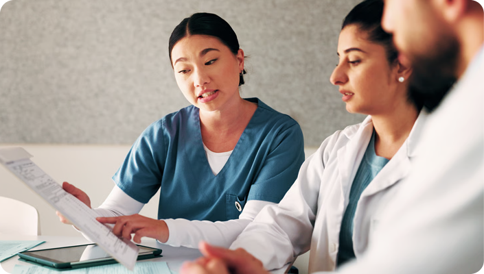 A nurse in teal scrubs and a doctor in a white coat reviewing a medical chart and a digital tablet together, representing hospice and home health billing compliance and revenue cycle management.