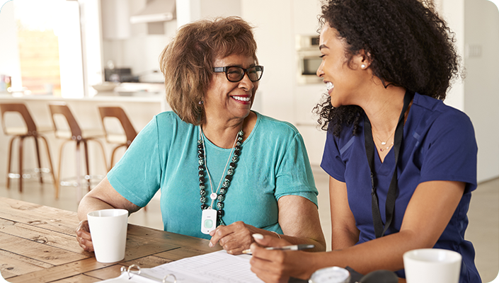 A hospice caregiver smiling and reviewing medical care documents with an elderly woman at a table, illustrating compliant hospice billing services.