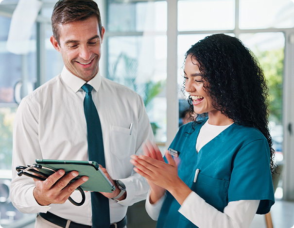 Healthcare administrator showing billing software results on a tablet to a smiling nurse in scrubs.